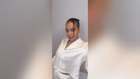 Smiling young woman in a white button-down shirt posing against a neutral wall in a bright, minimalist setting.