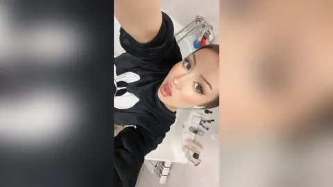 Young woman in a black graphic t-shirt taking a casual selfie in a bright white bathroom.