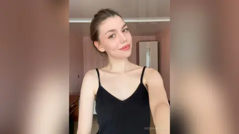 Smiling young woman in a black camisole tank top posing in a bright modern room.
