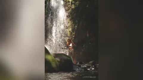 LaurentBelluci stands naked or in white bikini bottoms under a waterfall in a lush jungle setting.