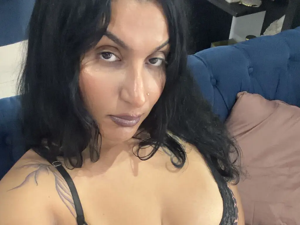 Close-up portrait of a woman with dark hair wearing a black lace bra in a cozy indoor setting.