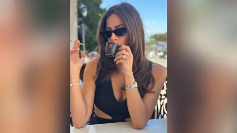 AnaMathers wears black sunglasses and a black tank top while holding a small black cup to her lips outdoors.