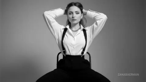 Elegant woman in white button-down shirt and black suspenders posing against a grey studio background.
