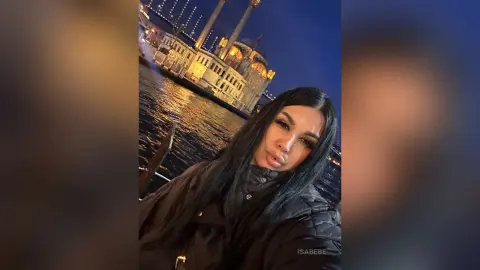 Young woman in a black puffer jacket enjoying a night out by a lit waterfront building.