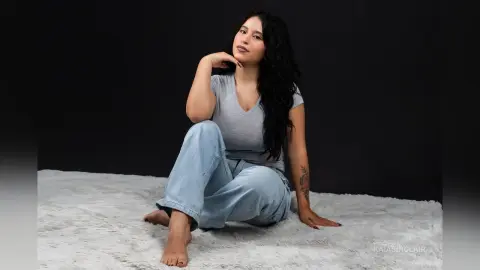 KaiaSinclair sits on a white shag rug wearing a grey v-neck shirt and light blue jeans.