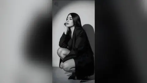 Elegant woman in a black blazer posing against a minimalist studio background in a moody black and white portrait.