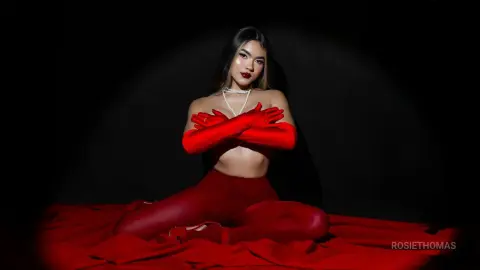 RosieThomas — Elegant woman in red evening gloves and matching outfit sitting on red fabric against a dark moody background.