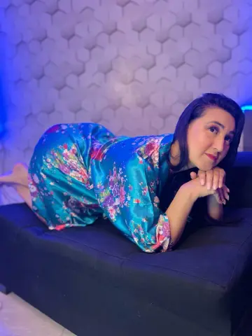 Smiling woman in a teal floral silk robe relaxing on a black sofa in a modern room with blue mood lighting.