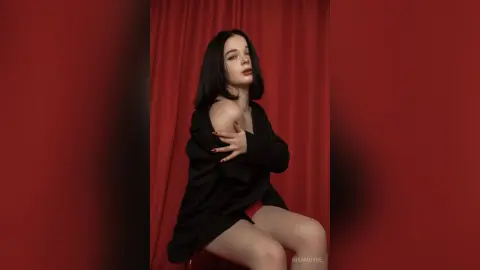 Elegant woman in a black blazer posing against red curtains in a moody, cinematic studio setting.