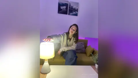 Young woman in a cozy beige sweater sitting on a sofa in a room with purple ambient lighting.