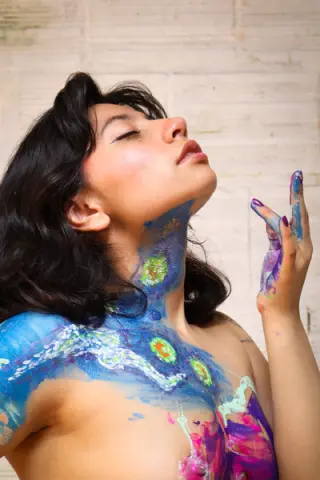 Dreamy portrait of a woman with colorful cosmic body paint against a white brick wall.