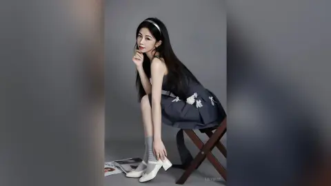 Elegant young woman in a dark navy floral dress and white heels sitting on a stool in a studio setting.