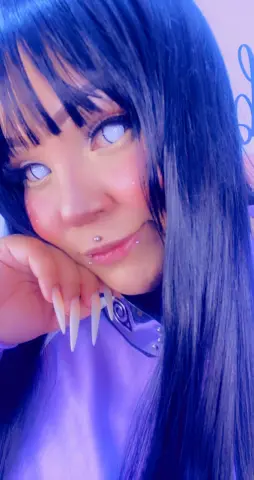 Cosplayer with long dark hair and light blue eyes wearing a purple outfit in soft blue lighting.