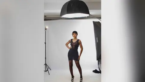 Elegant woman in a black lace bodysuit posing in a professional photo studio with soft lighting.