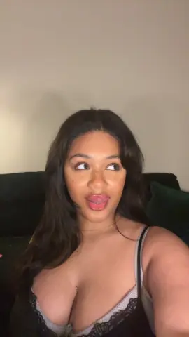 Hazelvalentine sticks her tongue out, wearing a black lace camisole with her long dark hair down while sitting on a dark green couch.