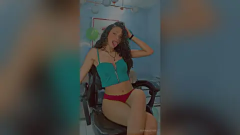 Playful young woman in a green crop top and red briefs posing in a modern living room.
