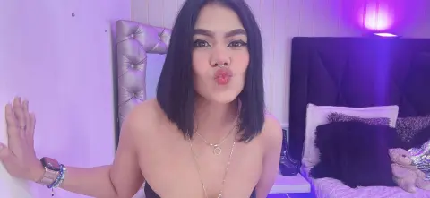 Young woman in a black top making a kissy face in a bedroom with purple mood lighting.