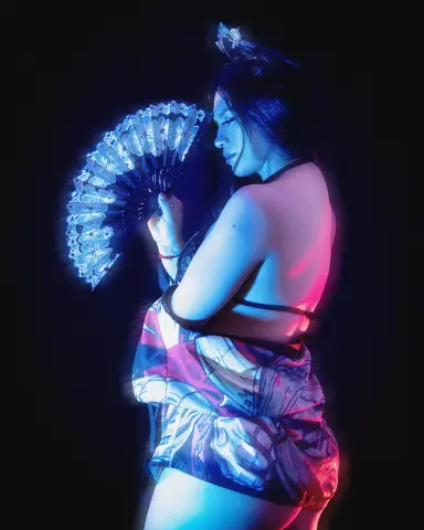 Woman in patterned kimono holding a glowing blue fan in a moody, cinematic dark setting.