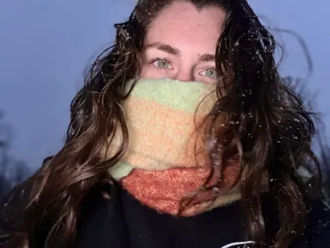 Woman with wavy hair wearing a cozy multicolored knit scarf in a cold winter setting.