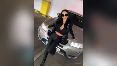 Stylish woman in black leather jacket and skinny jeans posing confidently against a silver BMW convertible.