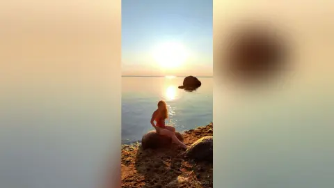 Woman in a red swimsuit sitting on a rock by the ocean during a peaceful golden hour sunset.