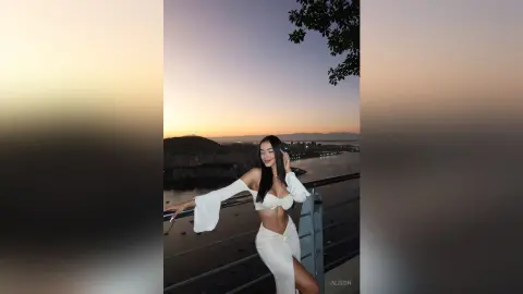 Alison poses outdoors at sunset wearing a white off-the-shoulder bra top and matching skirt.