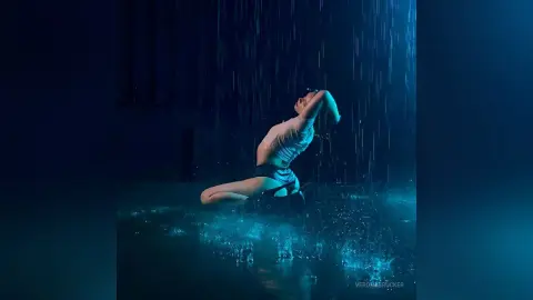VeronaBrucker poses naked in a heavy rain shower, arching her back while kneeling in the dark water.