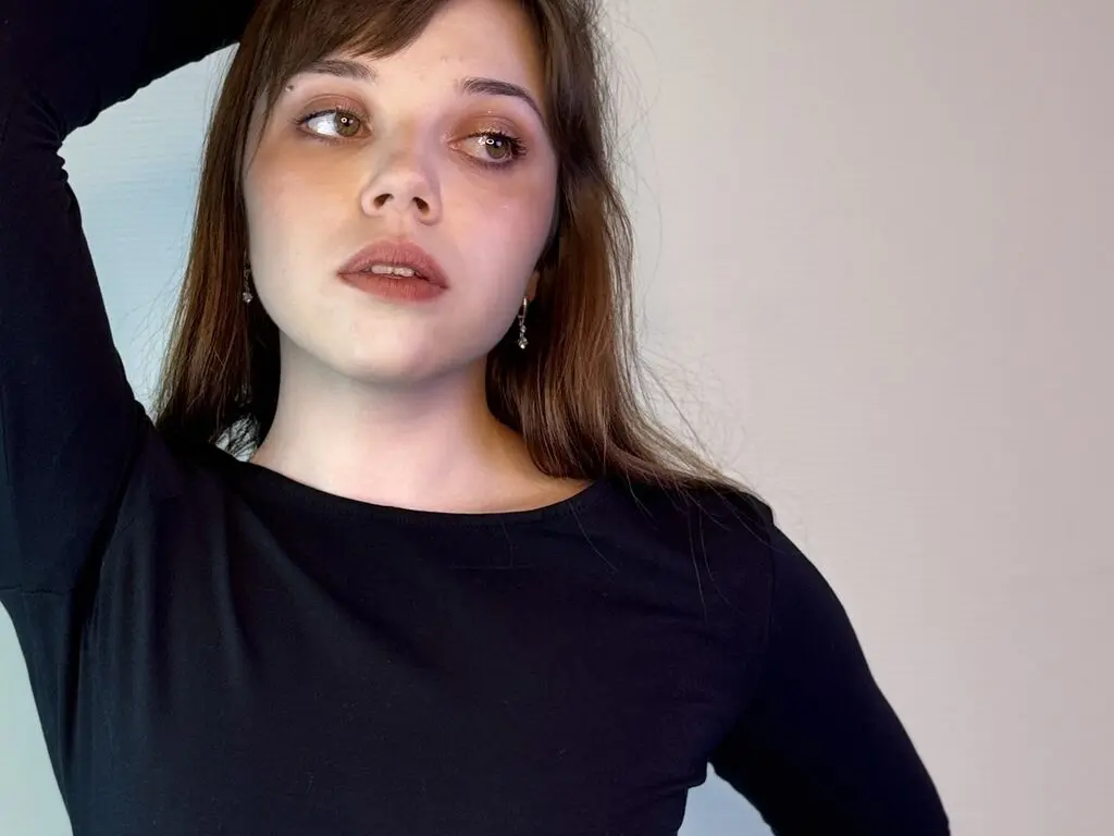 Young woman with brown hair wearing a black long-sleeve shirt against a neutral background with a thoughtful mood.