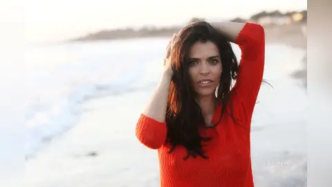 Beautiful woman in a red sweater posing on a sunny beach at sunset with a serene mood.