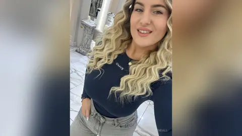 Smiling blonde woman in a navy blue long-sleeve shirt posing in a bright, modern marble hallway.