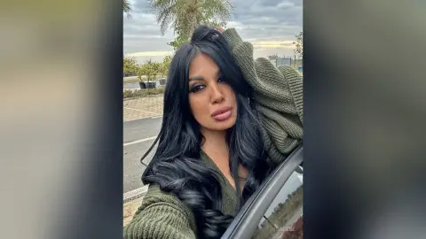 Woman with long dark hair wearing a cozy olive green sweater posing outdoors in soft natural light.