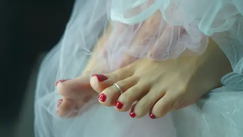 Close-up of bare feet with red nail polish resting on soft white tulle fabric in a dreamy, ethereal setting.