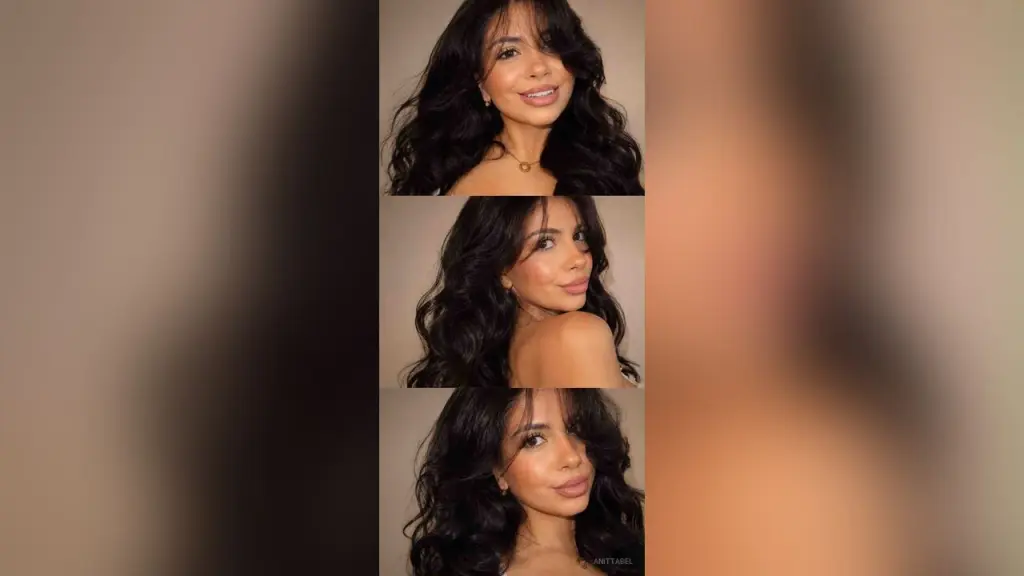 AnittaBel poses naked on a white floor, looking back over her shoulder with long wavy hair.