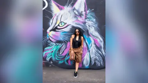 ChloeRiveiro — Stylish woman in black tank top and brown shorts standing before a colorful cat mural in an urban setting.