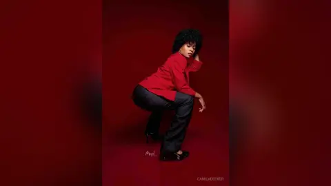 Stylish woman in a red long-sleeve shirt and black trousers posing against a moody red background.