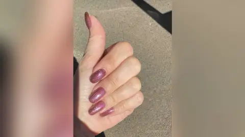 Close-up of a hand with sparkly pink glitter manicure nails in bright natural sunlight.