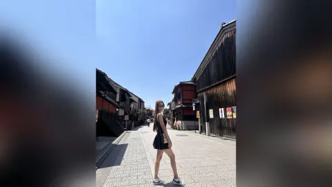 Stylish woman in a black summer dress walking through a traditional Japanese street under a clear blue sky.