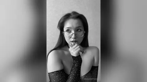 Moody black and white portrait of a woman in a sparkly black top wearing glasses and looking thoughtfully away.
