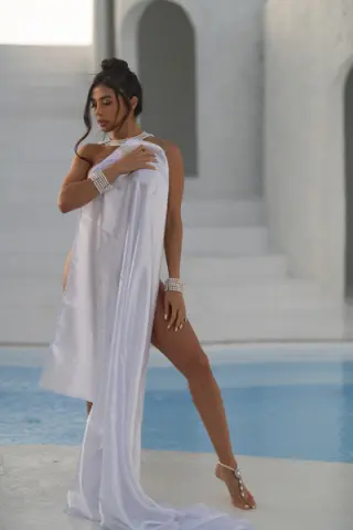 Elegant woman in a flowing white satin gown posing by a Mediterranean villa pool in a serene summer mood.