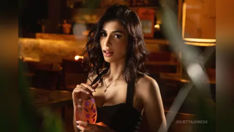 Elegant woman in a black dress holding a cocktail in a moody, dimly lit upscale lounge setting.