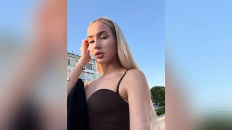 MarryDavies poses outdoors against a clear blue sky, wearing a black spaghetti-strap top with her long blonde hair down.