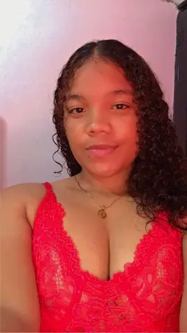 Smiling young woman with curly hair wearing a red lace camisole in a warm indoor setting.