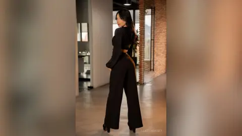 Elegant woman in black long-sleeve crop top and wide-leg trousers posing in a modern minimalist interior.