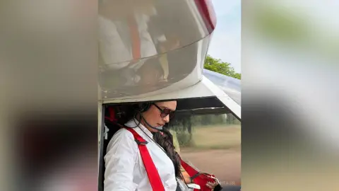MarianSajir wearing sunglasses and a white shirt sits inside a vehicle looking out the window.