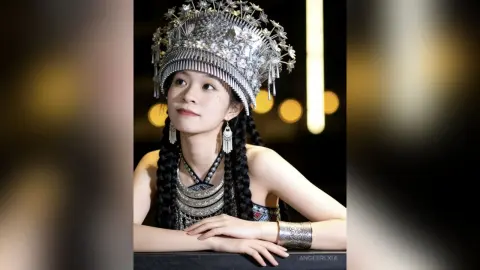 Young woman in ornate silver traditional ethnic costume and crown posing with a serene expression.