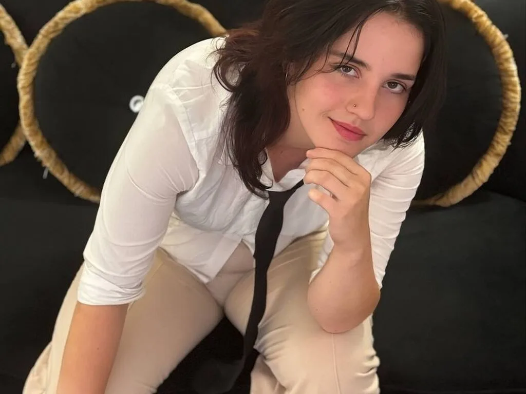 ZlataDouglas looks directly at the camera with a neutral expression, wearing a white collared shirt and small gold hoop earrings.