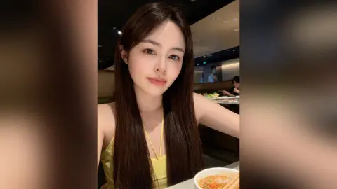 Young woman with long brown hair wearing a yellow tank top in a cozy restaurant setting.