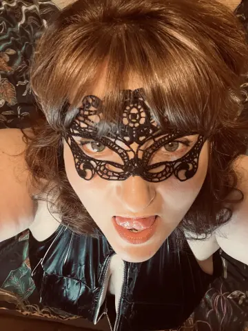 Woman in a black lace masquerade mask and leather outfit with a playful expression.