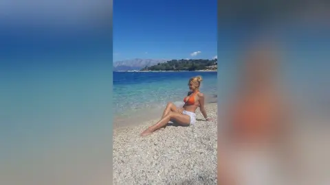 Blonde woman in an orange bikini relaxing on a sunny pebble beach by turquoise ocean water.