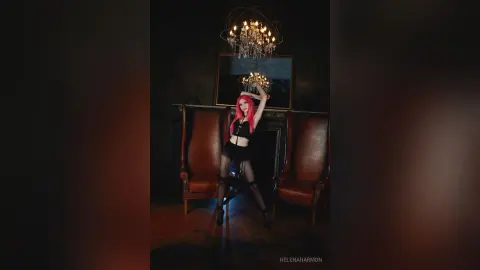 Woman with pink hair in a black corset outfit posing in a moody, dark vintage room under a crystal chandelier.